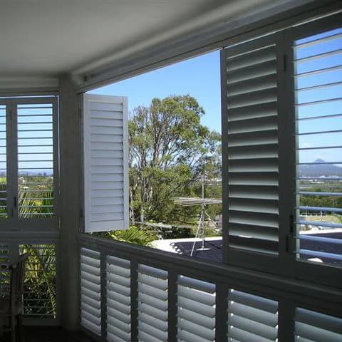 White aluminum plantation shutters installed on a balcony window with adjustable louvers.