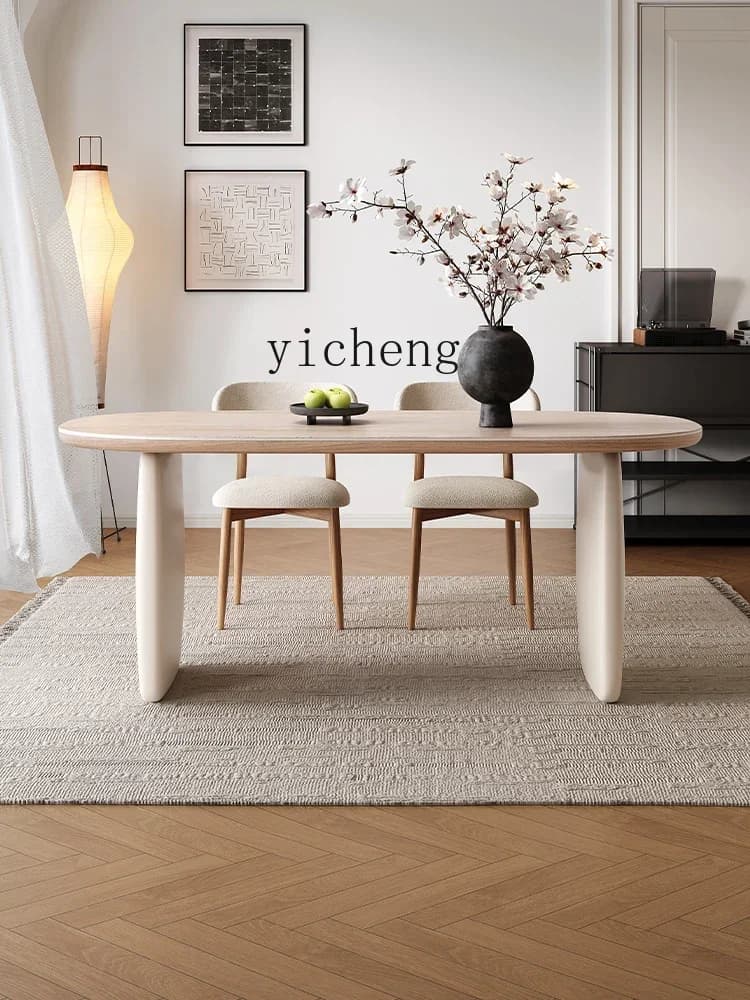 French cream oval dining table with a textured rock slab top and minimalist pedestal legs.