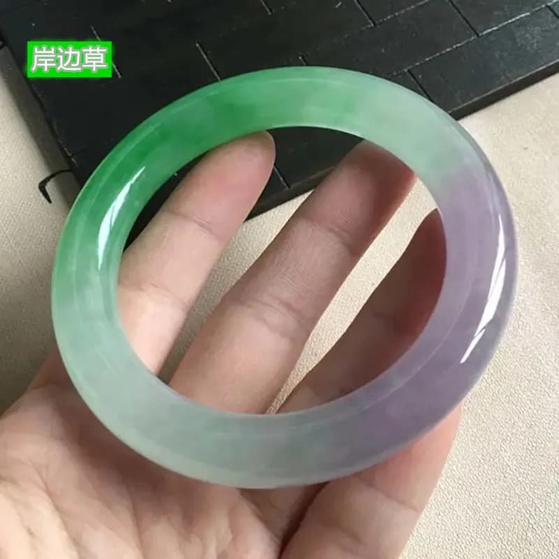 A hand holding a dual-toned Chuncai jadeite bracelet featuring soft violet and vibrant sun-green colors.