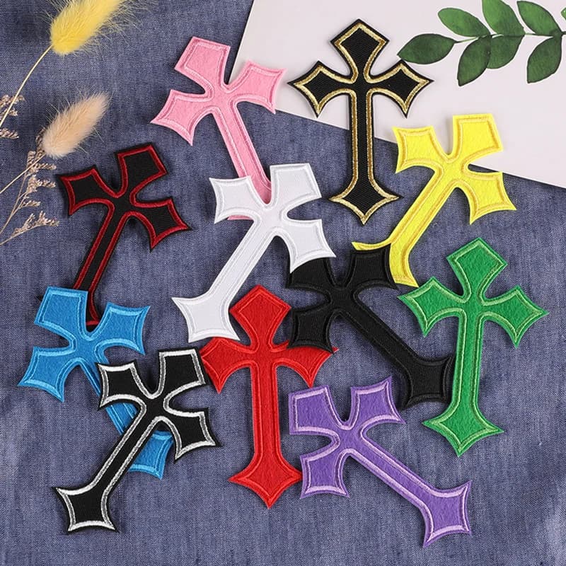 A variety of colorful embroidered cross patches spread out on a blue fabric surface.
