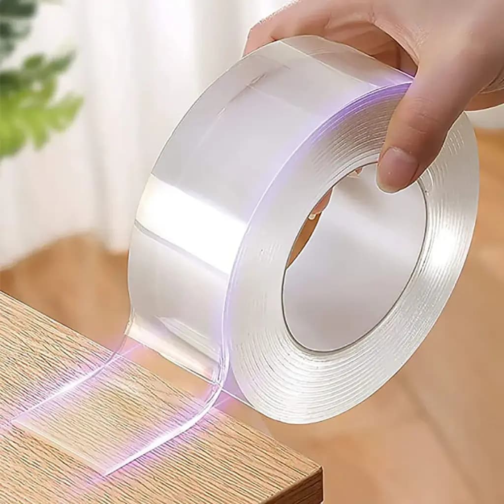 Roll of clear double-sided adhesive monster tape being applied to a wooden surface.
