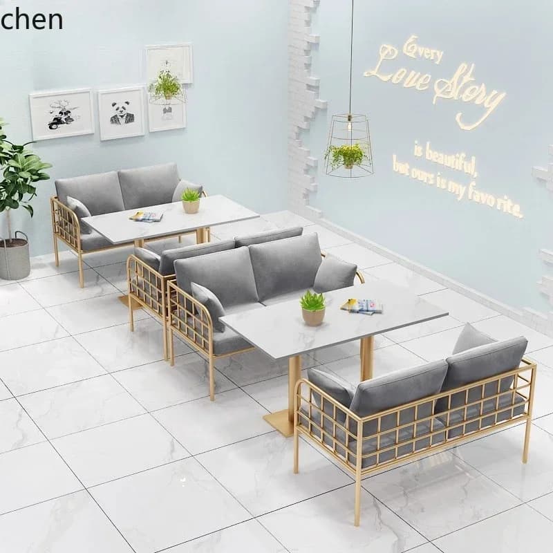 Modern gray velvet sofas and white marble-style tables with gold frames in a bright cafe setting.