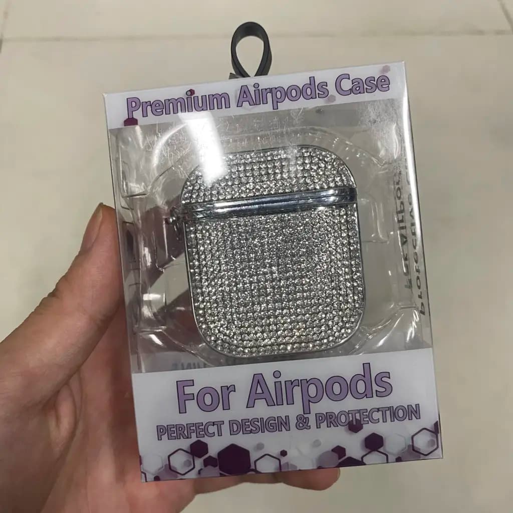 A sparkling silver diamond-encrusted protective case for Apple AirPods in its retail packaging.