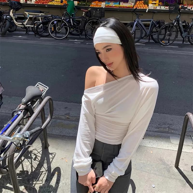 Woman wearing a white asymmetrical one-shoulder long sleeve top with ruched waist detail.