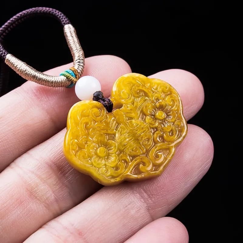 Intricately carved burnt yellow jadeite pendant featuring floral motifs and traditional fortune symbols.